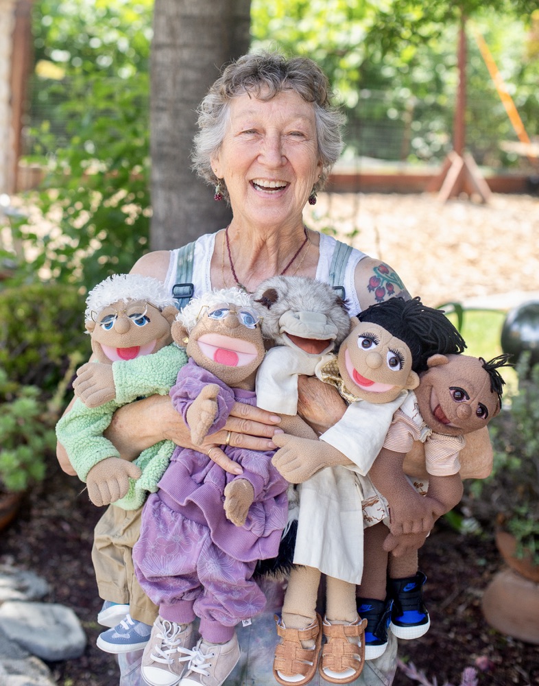 Carrie Elderberry laughing with an armful of puppets in her garden