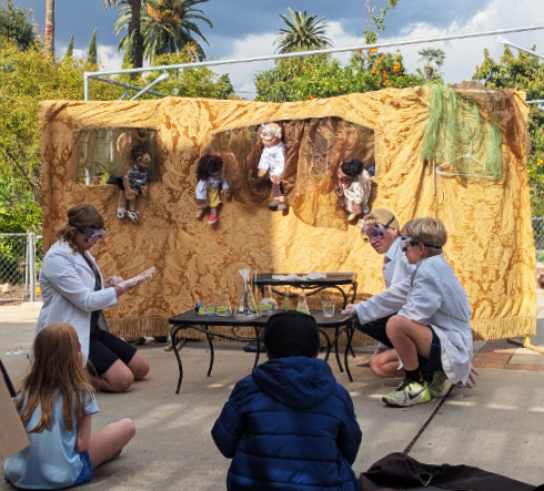 Children performing a science-themed puppet show in lab coats