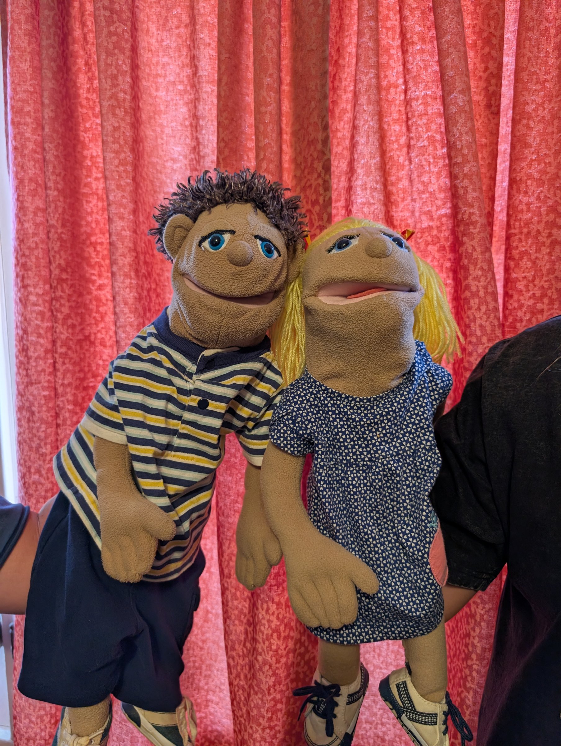 A boy and girl puppet pair against a red curtain