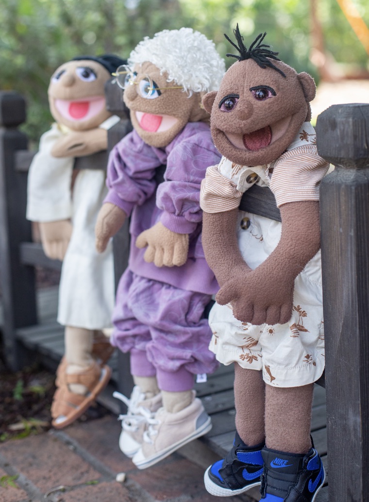 Three puppet characters leaning on a fence