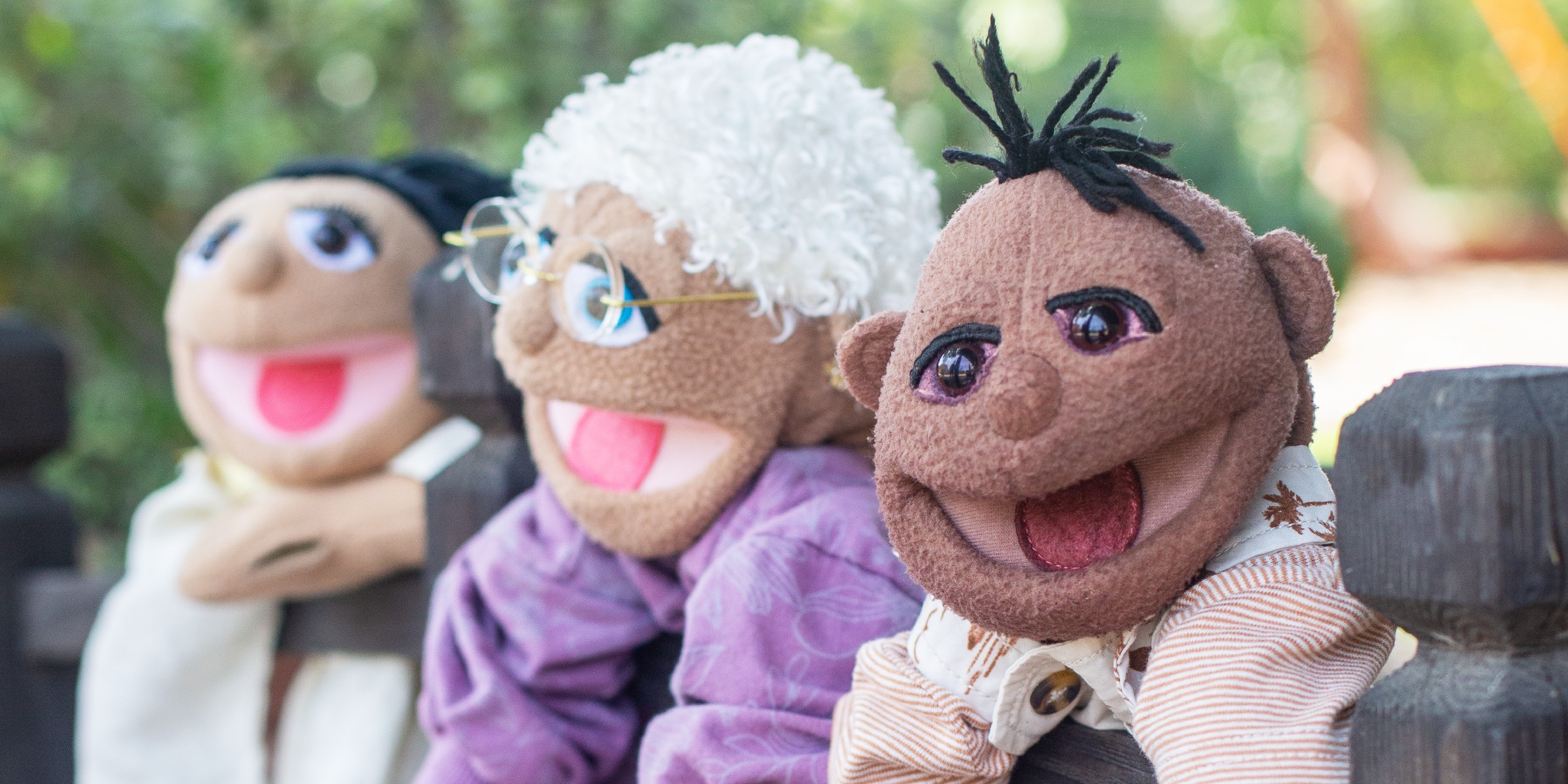 Three puppet characters leaning together on a garden fence